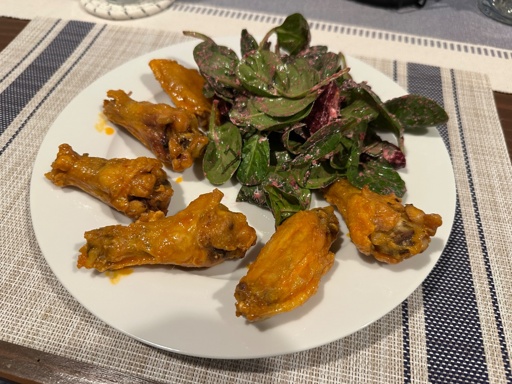 A line of chicken wings on a plate next to a salad